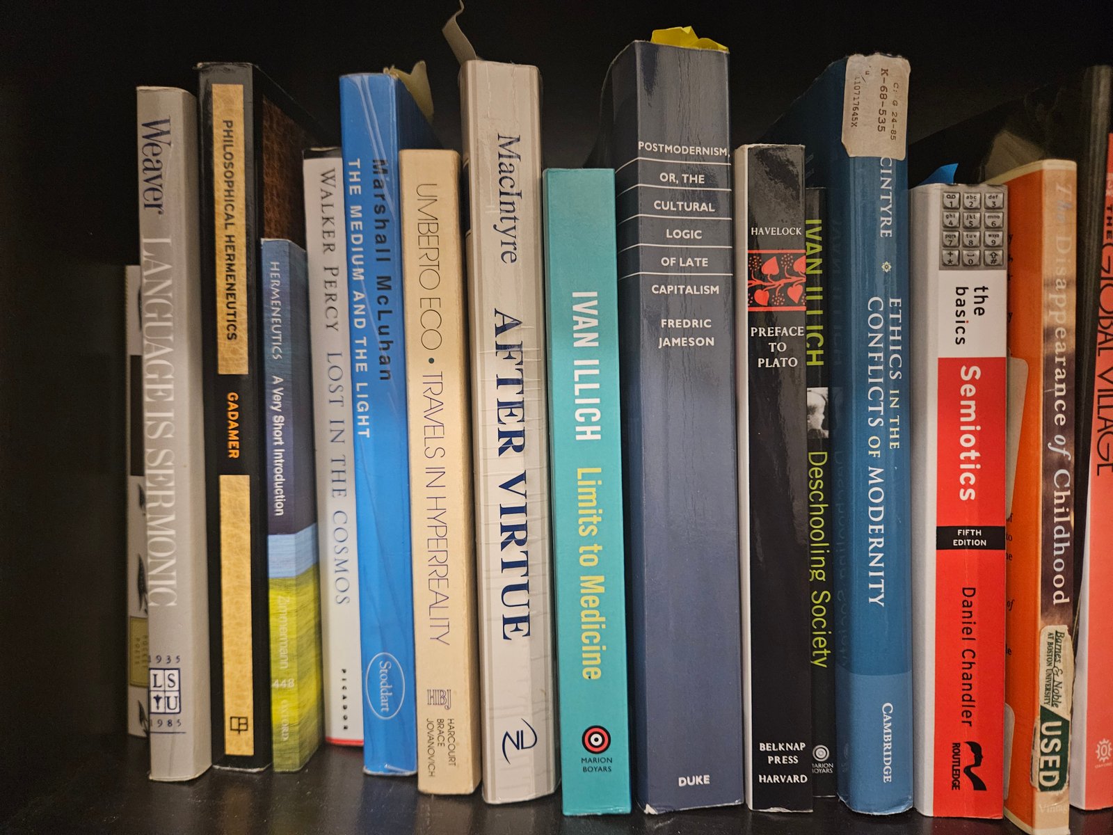 A bookshelf of works in rhetoric, media, and philosophy, including Walker Percy, Marshall McLuhan, and Ivan Illich.