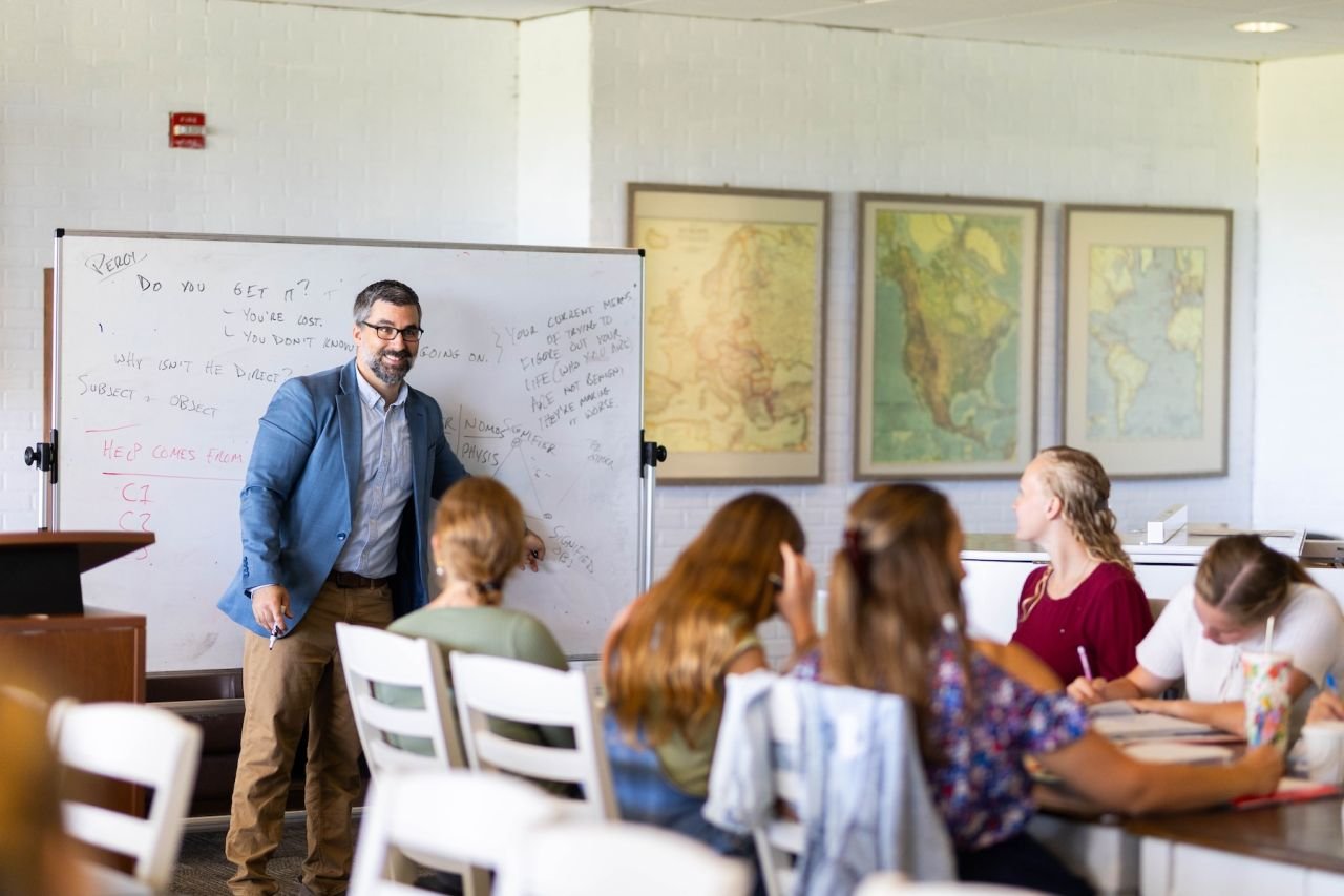 Justin N. Bonanno teaching at a whiteboard, with students seated nearby.